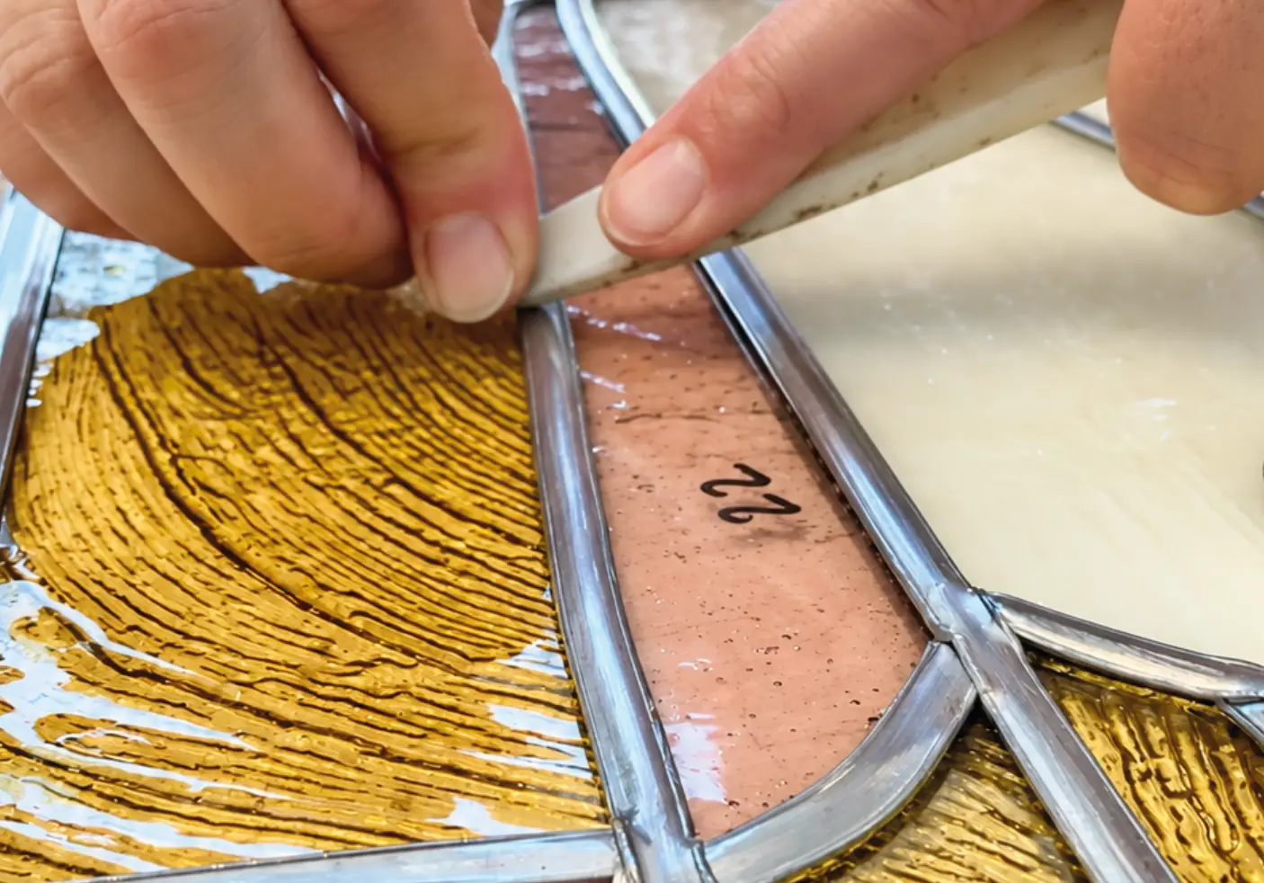 Mains assemblant des pièces de verre coloré avec des baguettes de plomb pendant un cours de vitrail